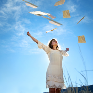 woman looking up to a blue sky with papers flying away