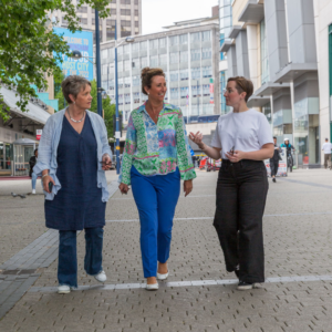 3 women walking towards the camera with tall buildings in background