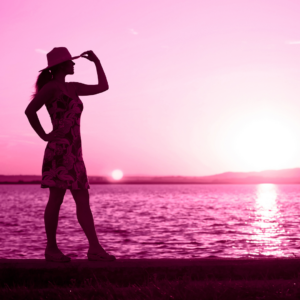 silouhette of a woman on a beach with a hat on. and pink background