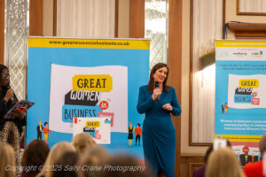 lady in blue dress standing on a stage with a microphone in front of a branded banner backdrop