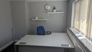 private office with grey desk and chair, shevling behind with plant and clock