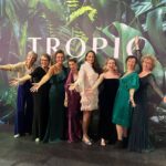 7 ladies in front of Tropic banner in evening dress