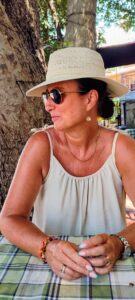 Sharon looking away from the camera in sunglasses and sun hat, sat across the table
