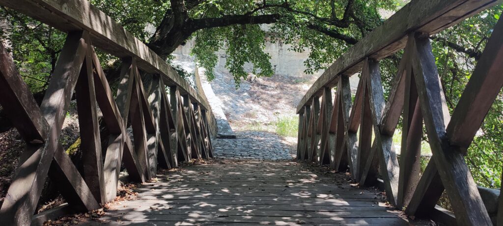 wooden ornate bridge leading to cobbled path and overhanging trees