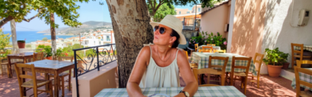 Sharon sitting in reflective mood in a restaurant in the Mediterranean wearing a sun hat and sunglasss